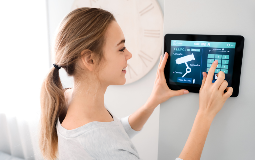 Woman using a smart home security system on a wall-mounted tablet, showcasing a product ideal for an eCommerce website.